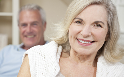 Older woman smiling with husband in background