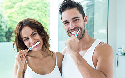 Two happy adults brushing their teeth together